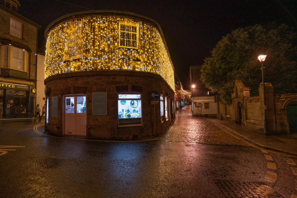 Night image of a rounded building draped in fairy lights, cobbled street