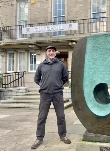 A man standing in front of a building next to a bronze sculpture