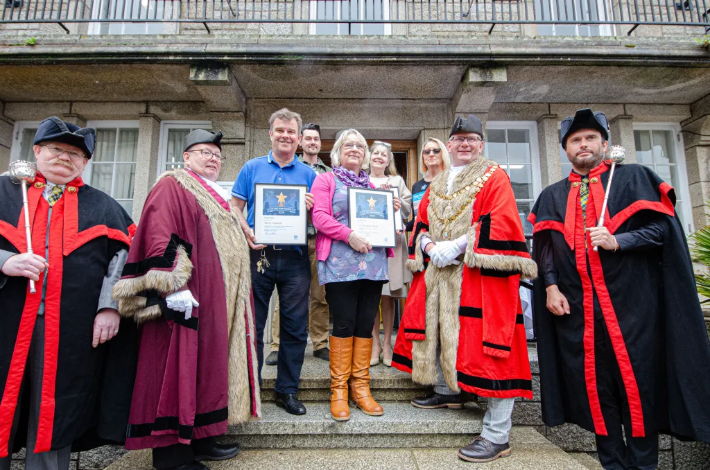 A group of men and women standing on steps. Some in civic regalia, e.g. cloaks and hats. Others holding framed certificates.